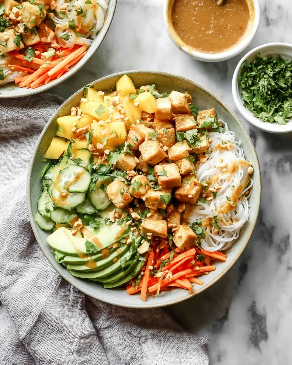 A white bowl filled with a colorful layered salad on a white marbled surface. The first layer is thick rice noodles, white and slightly translucent, covering the base. On top, bright orange shredded carrots are scattered along with thin slices of pale green cucumber. Cubes of golden-brown tofu are spread throughout, mixed with chunks of bright yellow mango. Thin slices of avocado with dark green skin and light green flesh fan out on one side. Small chopped peanuts and fresh green herbs are sprinkled over everything. A light brown dressing is drizzled on top, adding a glossy finish. Photo taken with an iphone --ar 4:5 --v 7