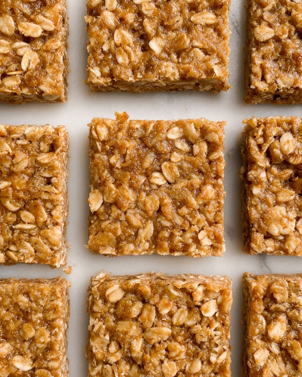 The image shows several square oat bars arranged neatly on a sheet with a white marbled texture. Each bar has a rough, crumbly surface with visible oats embedded in a light brown, slightly sticky base. The bars are thick and evenly cut, showing a dense texture with small oat pieces spread throughout. The close-up view highlights the coarse, grainy look of the oats contrasting with the smooth brown dough that holds them together. photo taken with an iphone --ar 4:5 --v 7