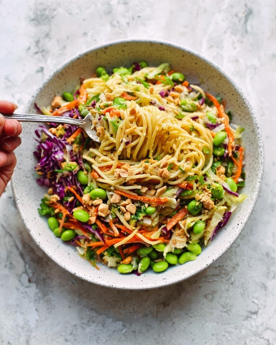 A bowl filled with a colorful mix of noodles, bright green peas, thin orange carrot strips, and light green avocado pieces. The noodles form the majority, with a pale yellow color and soft, tangled texture. Mixed throughout are small bits of scrambled eggs, adding a light golden layer. There are also some thin slices of purple cabbage peeking through, adding a touch of deep color. Fresh green cilantro leaves are scattered on top, along with white sesame seeds, giving it a fresh and slightly crunchy look. The bowl is white and sits on a white marbled surface, with soft natural light coming from the background. Photo taken with an iphone --ar 4:5 --v 7