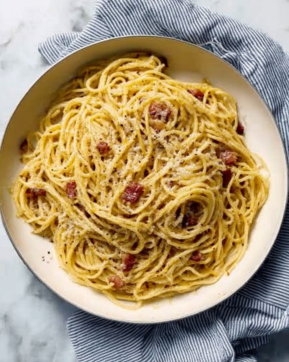A close-up view of a small mound of yellow spaghetti noodles twisted into a neat pile on a white plate, lightly coated in a creamy sauce, with fine white grated cheese sprinkled all over the top and around the base. Small dark red pieces are visible tucked among the noodles, adding contrast. The texture of the pasta is smooth and slightly glossy, and the white plate contrasts with the creamy pasta, placed on a white marbled surface. photo taken with an iphone --ar 4:5 --v 7