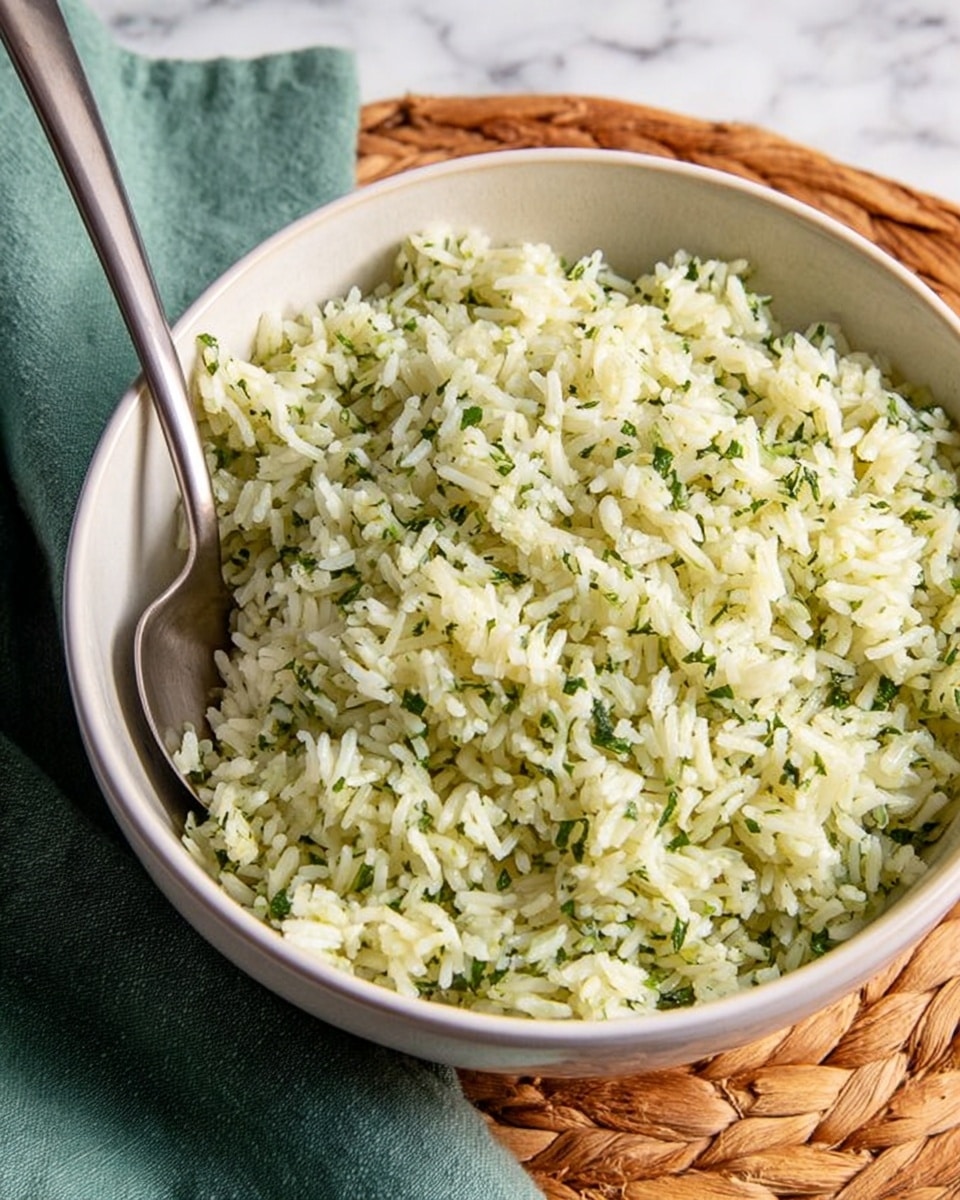 A white bowl filled with cooked rice mixed with finely chopped herbs, giving the rice a light green speckled look, and garnished with fresh parsley leaves on top. A gold spoon rests on the right edge of the bowl, partially inside the rice. The bowl sits on a white marbled surface with a white napkin featuring a lace trim placed casually beside it. Photo taken with an iphone --ar 4:5 --v 7