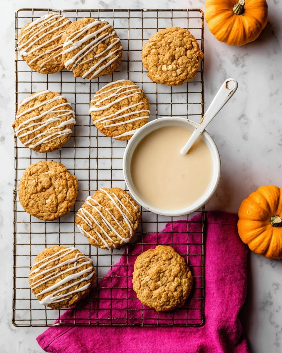 The image shows seven round cookies with a light golden-brown color and a slightly crumbly texture. Each cookie is topped with wavy white icing drizzled evenly across the surface. The cookies rest on a silver cooling rack placed on a bright magenta cloth with a small orange pumpkin nearby. The scene is set on a white marbled surface. The overall look is warm and cozy, with a mix of soft cookie texture and smooth icing. Photo taken with an iphone --ar 4:5 --v 7