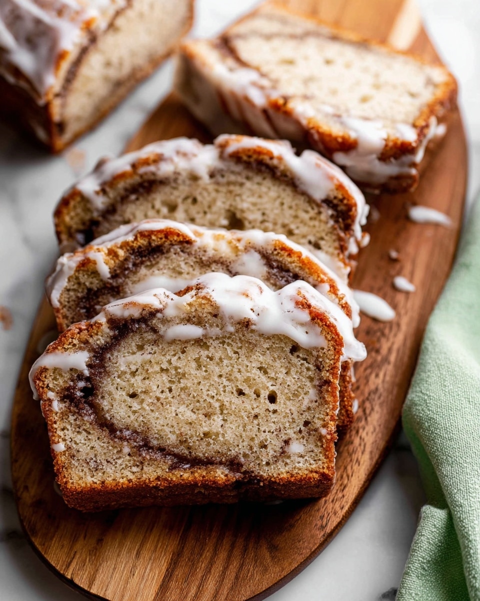 A close-up view of a sliced banana bread loaf resting on a wire rack over a wooden board, showing its dense, moist texture with small dark specks throughout and a swirled dark brown cinnamon layer running through the middle, topped with thin white icing drizzled in lines across the top ridges, all placed on a white marbled surface photo taken with an iphone --ar 4:5 --v 7