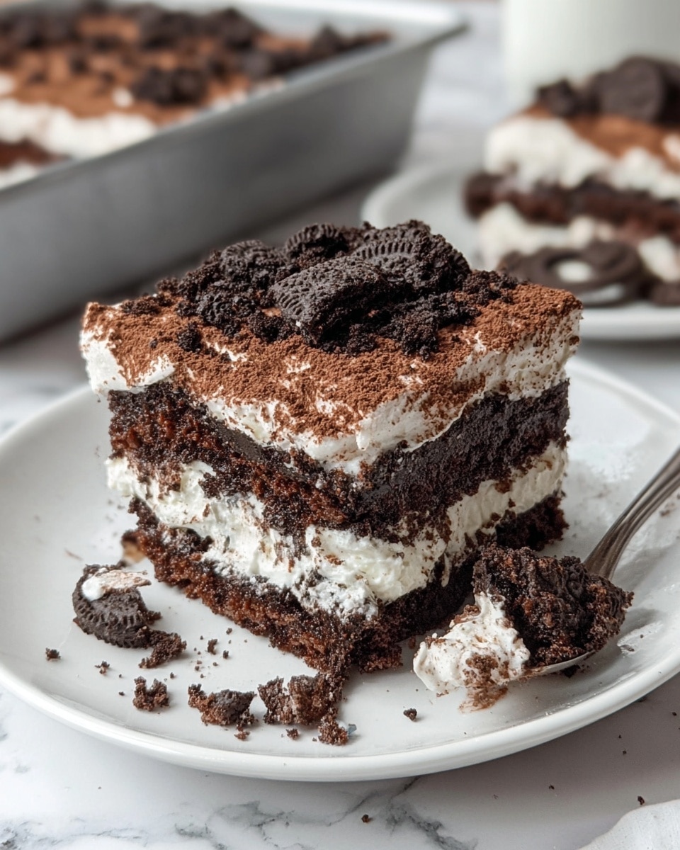 The image shows a square chocolate dessert with two main layers inside a metal baking pan on a white marbled surface. The bottom layer is a moist, dark brown cake with a slightly crumbly texture. Above it is a thick white cream layer that looks smooth and soft. The top is dusted with a light brown cocoa powder and scattered with small, crushed dark chocolate cookie pieces. Three squares of the dessert are left intact, while one square is missing from the front corner, showing the layers inside. Some crumbs and small drops of liquid are visible on the pan. Photo taken with an iphone --ar 4:5 --v 7