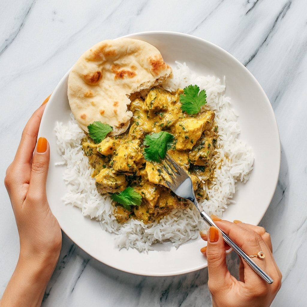 A white bowl holds a colorful dish with three main layers arranged side by side. The bottom layer on the left is fluffy, white rice with visible grains and sprinkled with small pieces of green herbs. Next to the rice, there are slices of ripe avocado, fanned out, showing a smooth creamy texture and pale green color with a darker green edge. Covering the right side of the bowl is a creamy orange sauce with grilled chicken pieces on top. The chicken is cut into cubes, browned with char marks, and mixed with finely chopped green herbs and small red chili bits, giving a fresh and spicy look. The bowl sits on a white marbled surface with blurred green herbs in the background. Photo taken with an iphone --ar 4:5 --v 7