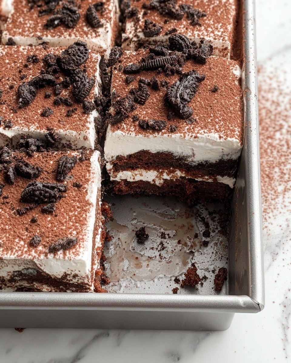 A three-layer dessert slice sits on a white plate with a white marbled surface underneath. The bottom and middle layers are dark chocolate cake, soft and moist in texture. Between these cake layers and on top is a creamy white filling that looks light and fluffy. The top is dusted with cocoa powder and covered with crushed dark chocolate cookie pieces, adding a rough, crumbly texture. Some crumbs are scattered around the plate, and in the background, more pieces of the cake and cookies are visible, along with the edge of a silver baking pan. Photo taken with an iphone --ar 4:5 --v 7
