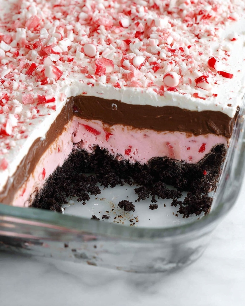 The image shows a thick square dessert on a white plate with three distinct layers. The bottom layer is dark and crumbly, looking like crushed cookies or chocolate crust. The middle layer is light pink with a soft, creamy texture, and small bits can be seen inside it. The top layer is a smooth, thick dark chocolate, covering the pink layer fully. On top, there is a thick layer of white cream with small, crushed red and white candy pieces spread evenly, adding color and texture. The background is a white marbled surface with faint holiday decorations blurred out. Photo taken with an iphone --ar 4:5 --v 7