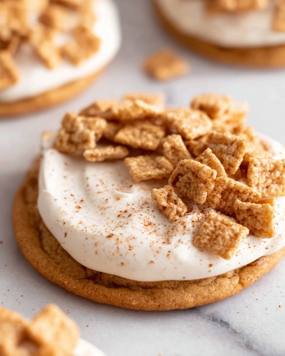 Four round cookies each with two layers: a base layer of golden brown cookie, topped with a thick, smooth swirl of white cream. On top of the cream, there are several small, square cereal pieces in light brown with a dusting of cinnamon sugar, some scattered around the cookies. The cookies are on a white marbled surface with a jar of cinnamon maple sugar spice on the side, its copper-colored lid placed next to it. photo taken with an iphone --ar 4:5 --v 7