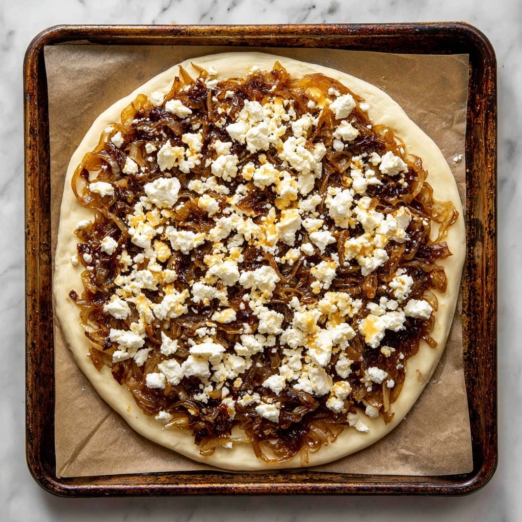 A rectangular sheet of pale uncooked dough lies flat on a baking tray lined with parchment paper, topped evenly with a thick layer of dark golden-brown caramelized onions that have a soft, slightly glossy texture, spread close to the edges but leaving a small border of dough visible. Over the onions is a generous scattering of crumbly, bright white feta cheese pieces, unevenly broken into small and medium chunks, which contrast sharply with the dark onion base. The baking tray shows some wear with darkened edges, and the whole setup rests on a white marbled surface. Photo taken with an iphone --ar 4:5 --v 7