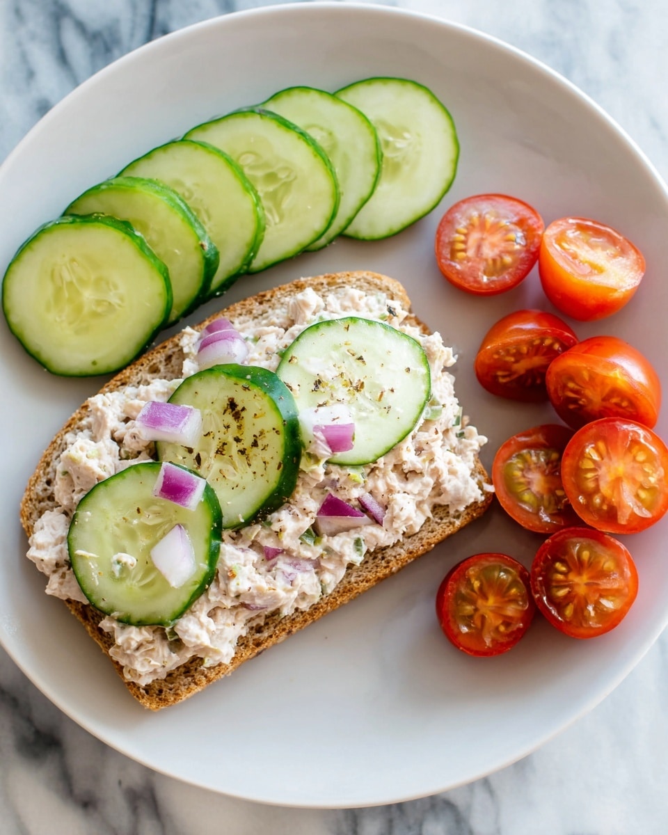 The image shows a sandwich cut in half and stacked on a white square plate with a textured surface. The sandwich has three layers: two slices of brown wheat bread that are lightly toasted, a middle layer of light chicken salad mixed with small green herbs and mayonnaise, and a thin layer of fresh green lettuce at the bottom. The sandwich looks soft and fresh, and it sits on a white marbled surface with a clear glass of water in the background. photo taken with an iphone --ar 4:5 --v 7