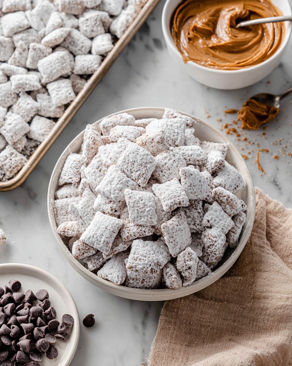 A close-up side view of a white bowl filled with many small square cereal pieces covered in a thick dusting of white powdered sugar. Behind it, a baking tray holds many more of these cereal squares coated in powdered sugar. To the right, a white bowl contains smooth brown peanut butter, with a spoon resting inside. To the left, a white plate has a small pile of dark chocolate chips, with some scattered on the soft beige cloth under the bowl and plate. All items rest on a white marbled surface. Photo taken with an iphone --ar 4:5 --v 7