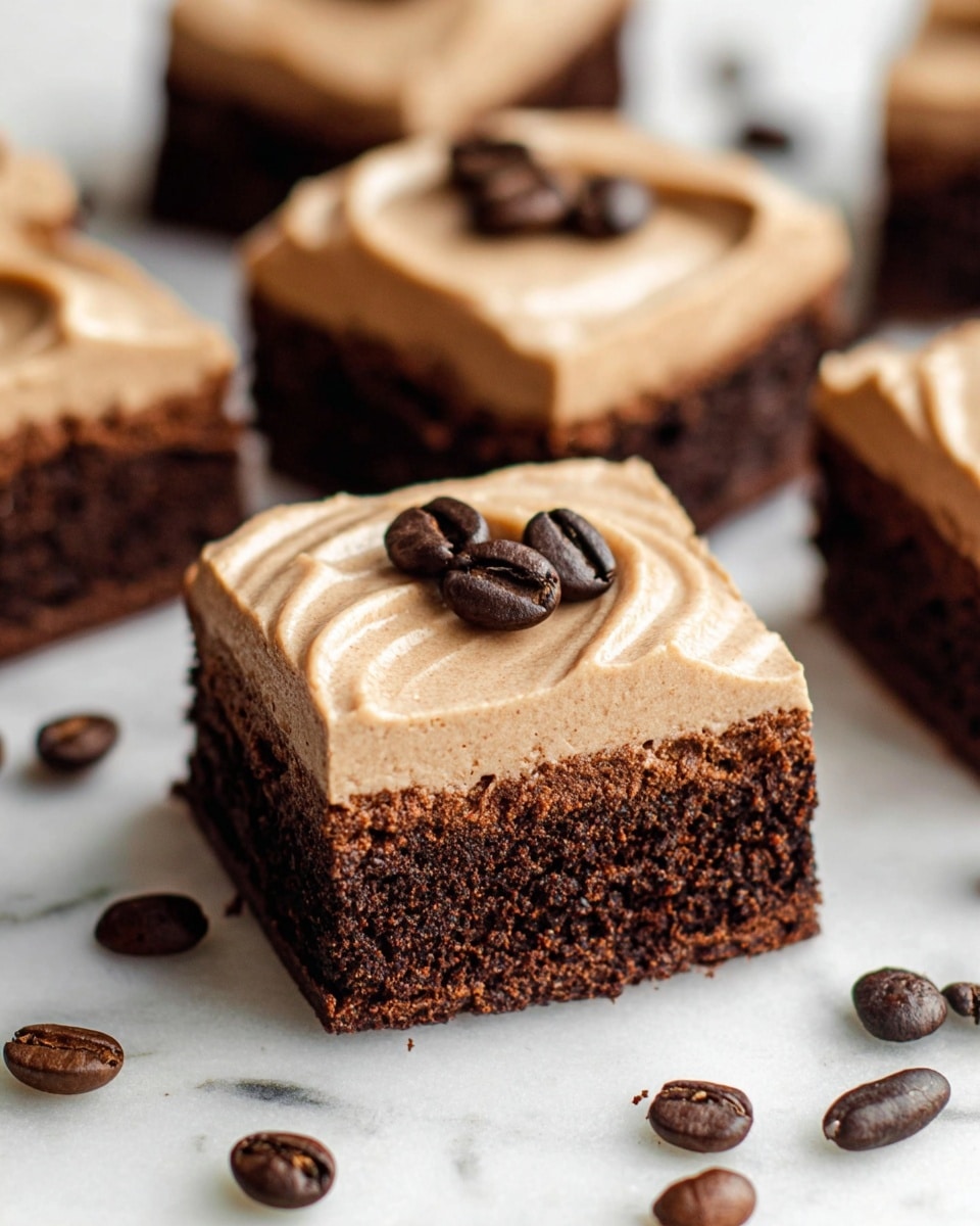 The image shows three square brownies stacked on a white marbled surface. Each brownie has two layers: the bottom layer is dark chocolate and dense with a moist texture, and the top layer is a smooth, light brown coffee-flavored frosting with soft ridges. On top of the frosting of two brownies, there are three glossy coffee beans. One brownie has a bite taken out of it, revealing the rich chocolate interior. Around the brownies, there are scattered dark roasted coffee beans that add detail and depth to the scene. Photo taken with an iphone --ar 4:5 --v 7