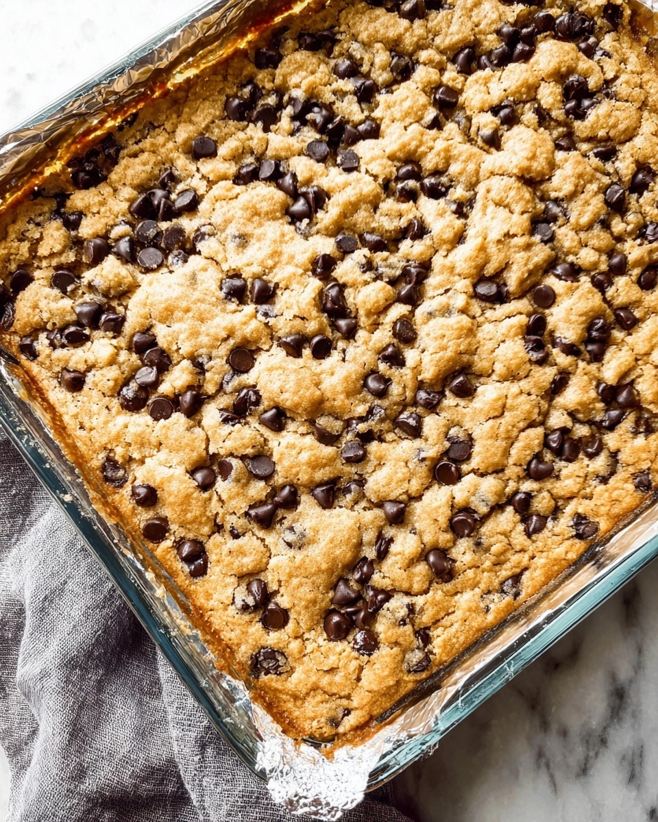 The image shows four square dessert bars on a white plate, each with three visible layers. The bottom layer is brown and crumbly, like a cookie or graham cracker crust. The middle layer is thick, smooth, and white, resembling a creamy filling. The top layer is chunky and beige with dark brown chocolate chunks mixed in, giving a cookie-dough look. Two loose chocolate chips lie next to the nearest square on the plate. The background is a white marbled surface, and the focus is on the front bar, with the others slightly blurred in the back. photo taken with an iphone --ar 4:5 --v 7