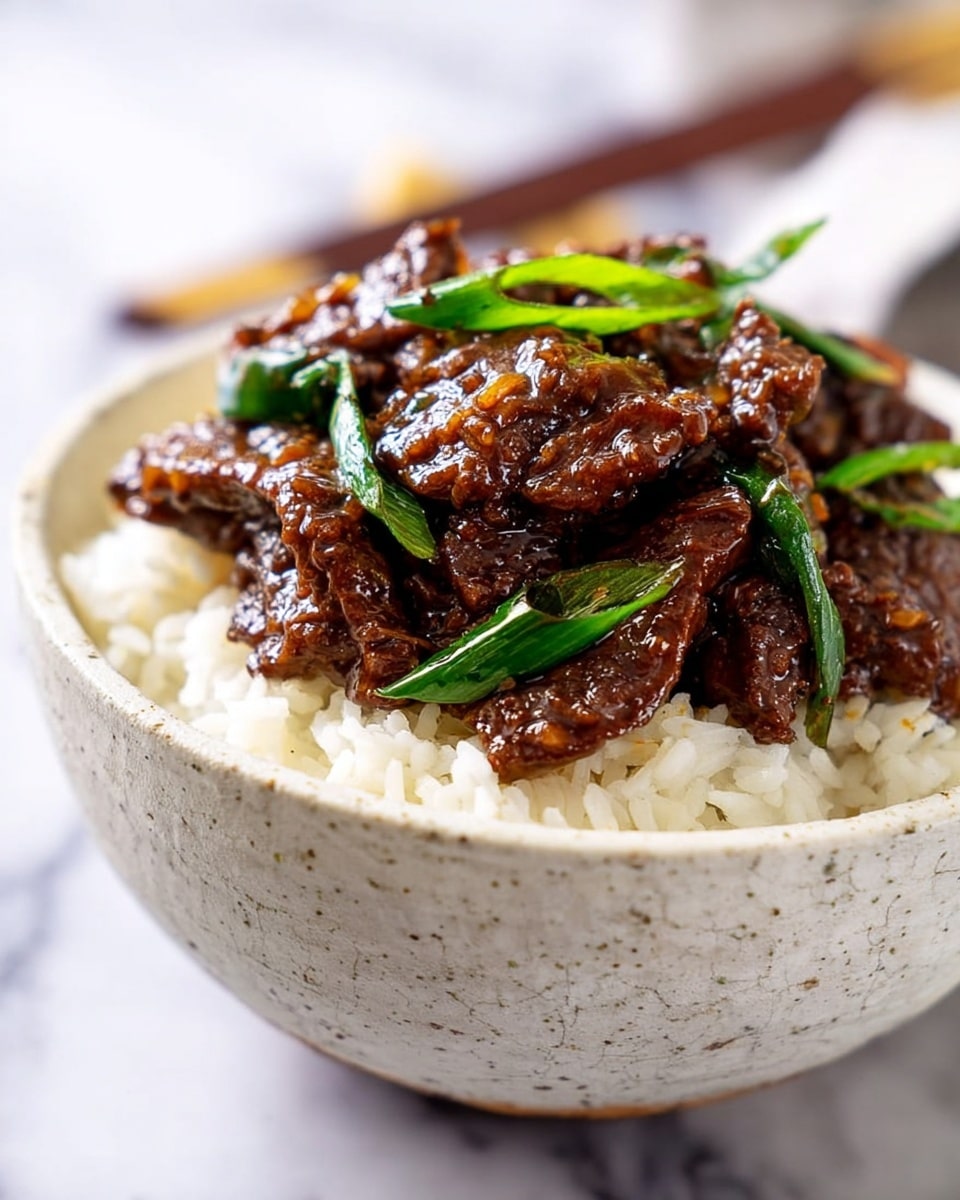 The image shows a white bowl filled with a rich, glossy beef stir-fry that has about two main layers. The bottom layer is made of tender, thinly sliced brown beef pieces cooked to a soft, juicy texture coated in a shiny dark brown sauce. The top layer includes scattered bright green onion pieces adding a fresh, slightly crunchy contrast. The beef looks well coated with a thick sauce that glistens under the light, making the dish appear very flavorful. The bowl is placed on a white marbled surface, creating a clean and simple background. photo taken with an iphone --ar 4:5 --v 7