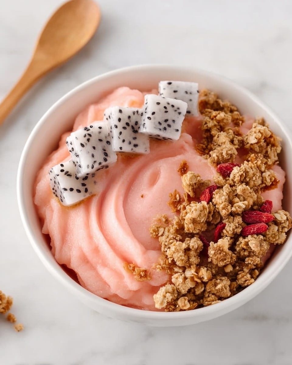 A white bowl filled with smooth, creamy light pink frozen yogurt as the base layer, topped with a neat row of cubed white dragon fruit with small black seeds on the left side, and a sprinkle of golden-brown crunchy granola mixed with a few small red dried berries placed next to the fruit, all set on a white marbled surface with a wooden spoon placed to the left of the bowl and two smaller white bowls partially visible on the right side containing granola and cubed dragon fruit. photo taken with an iphone --ar 4:5 --v 7