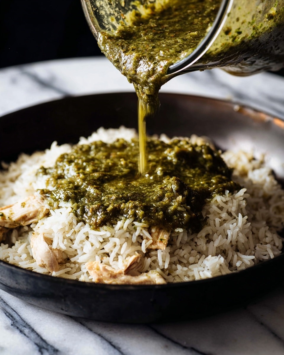 A large gray pan is filled with a cooked dish that has three visible layers: a base layer mixed with shredded chicken, black beans, yellow corn, and rice, all covered by a melted light beige cheese layer with some herbs scattered throughout; on top, there are two slices of bright green avocado placed side by side, each sprinkled with finely chopped fresh green cilantro and a few red chili flakes. The pan rests on a wooden table with a small white bowl of chopped cilantro nearby and a white cloth on the right edge. A window with natural light shines in the background, and the whole scene sits on a white marbled surface. Photo taken with an iphone --ar 4:5 --v 7