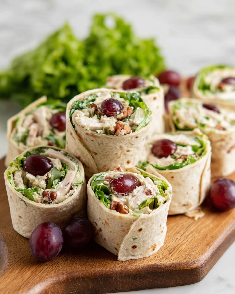 The image shows several wrap pinwheels cut into thick rounds and placed on a wooden board. Each wrap has three main visible layers: a light beige tortilla on the outside, a creamy white filling mixed with small bits of pecans and green leafy lettuce in the middle, and dark red grape slices on top, adding a pop of color and freshness. The wraps are arranged in a casual pile with extra green lettuce leaves in the background on a white marbled surface. Two whole grapes are placed near the board, adding contrast. The texture of the tortilla is soft with tiny brown specks, the filling is creamy and slightly chunky, and the grape slices have a glossy finish. photo taken with an iphone --ar 4:5 --v 7