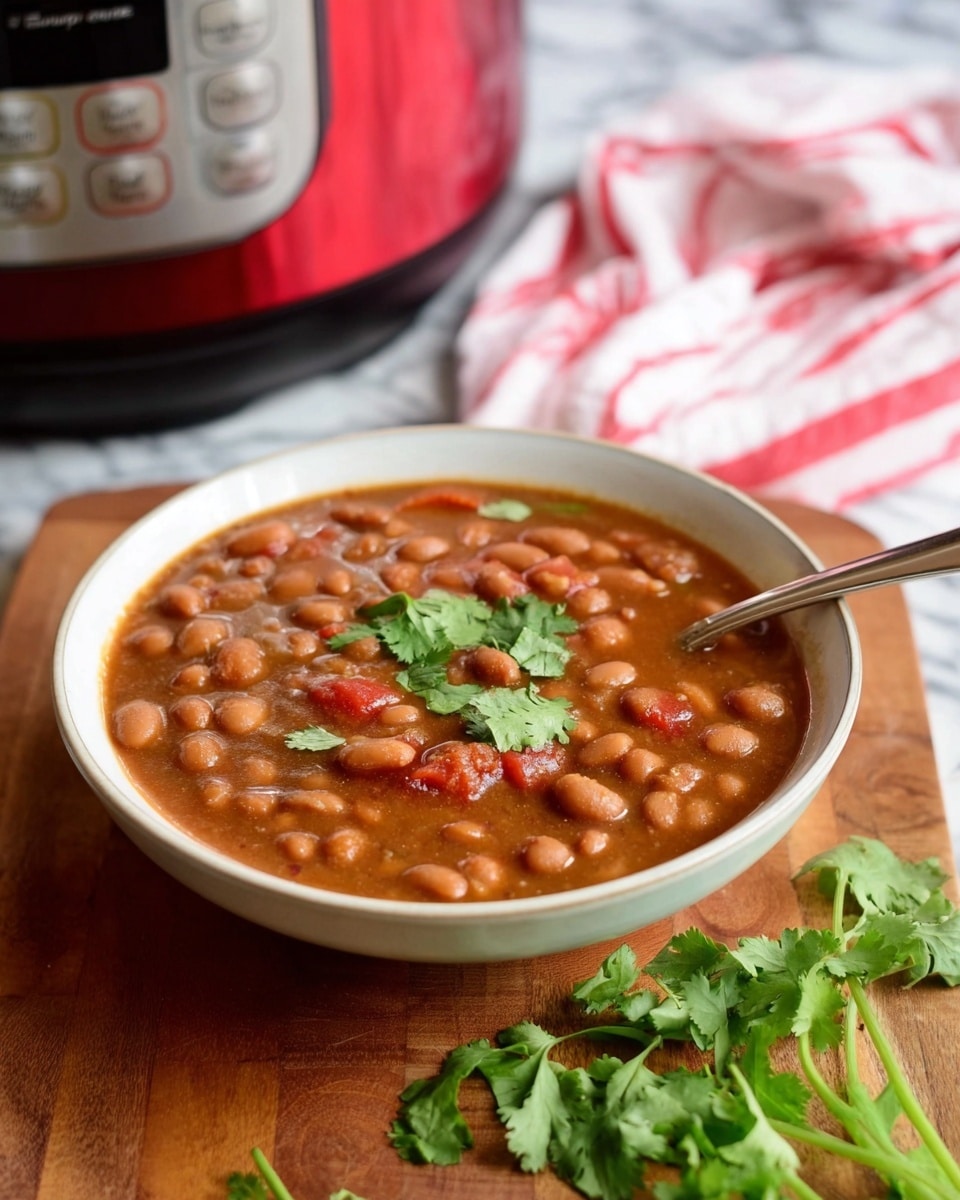 A bowl of bean stew is shown in a shallow white bowl filled with a thick brown broth, containing many small light brown beans and some pieces of red tomato, garnished with a few green cilantro leaves scattered on top. A spoon rests inside the bowl on the right side. The bowl sits on a wooden surface with some green cilantro stems nearby. Behind the bowl, there is a red Instant Pot and a white cloth with red stripes, all set against a white marbled background. photo taken with an iphone --ar 4:5 --v 7